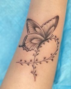 a black and white butterfly tattoo on the left arm, with small flowers around it