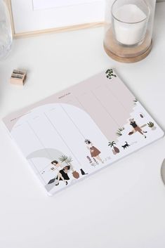 a white desk with a pink planner on it and a glass of water next to it