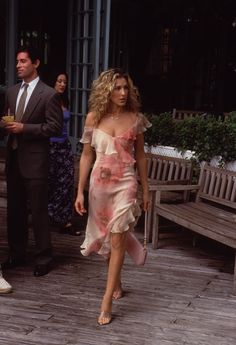 a woman in a pink dress walking down a wooden walkway with two men standing behind her