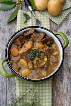 a bowl of beef stew with potatoes and carrots on a green checkered napkin