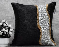 a black and silver pillow sitting next to a white vase filled with flowers on top of a table