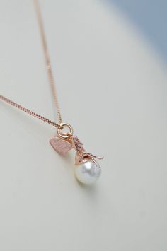 a gold necklace with a pearl and a bee charm on the front, sitting on a white surface