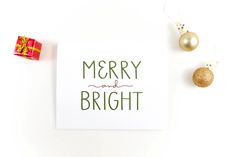 a merry and bright christmas card next to ornaments on a white background with gold balls