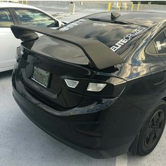 an electric car parked in a parking lot next to another car with its hood up