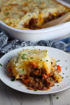 a white plate topped with lasagna covered in meat and cheese next to a casserole dish