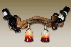 three wine glasses with red and orange liquid in them hanging from a wooden holder on a wall