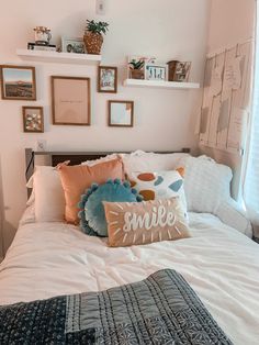 a white bed topped with lots of pillows next to a wall filled with framed pictures