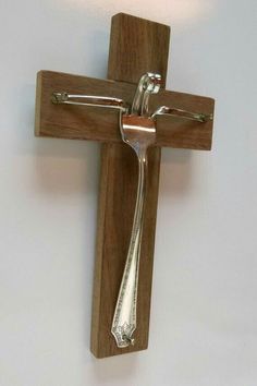 a wooden cross with a spoon hanging from it's side on the wall next to a light