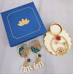 two pairs of earrings sitting next to a blue box on a white tablecloth covered surface