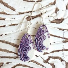 two purple and white earrings hanging from silver earwires on a piece of wood