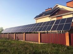 a house with solar panels on the roof and in front of it is a red fence