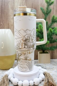 a white coffee mug sitting on top of a table next to a vase and pine cones