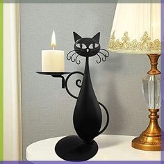 a black cat candle holder on a table next to a lit candle and a lamp