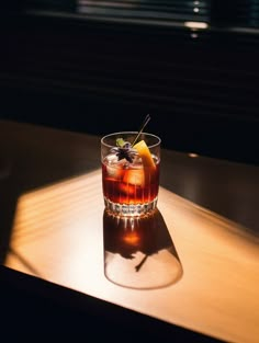 a glass filled with liquid sitting on top of a wooden table next to a window