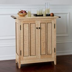 a wooden cabinet sitting on top of a hard wood floor next to a bowl of fruit