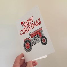 a hand holding up a christmas card with an image of a red tractor on it