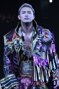 a man dressed in an elaborately designed outfit on stage with his hands behind his back