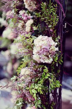 flowers are growing up the side of a pole in front of some bushes and trees