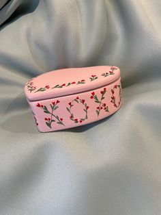 a pink box with red flowers on it sitting on a white cloth covered bed sheet