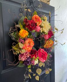 a wreath is hanging on the front door with flowers and greenery around it,