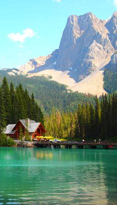 a lake surrounded by trees and mountains with a house on the dock next to it