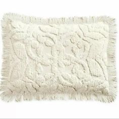 a white pillow with fringes on the bottom and an embroidered design in the middle