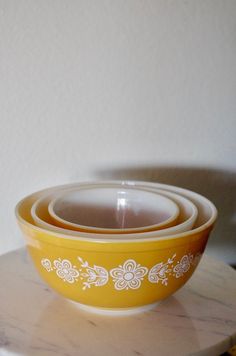 three yellow and white bowls sitting on top of a marble table next to each other