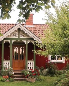 a red house with green trim and white trim on the front door is surrounded by greenery