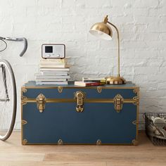 a blue trunk sitting on top of a wooden floor next to a bike and lamp