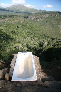 a bathtub sitting on top of a rock next to a lush green hillside