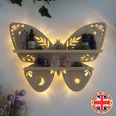 a butterfly shaped shelf with candles and bottles on it's shelves next to flowers