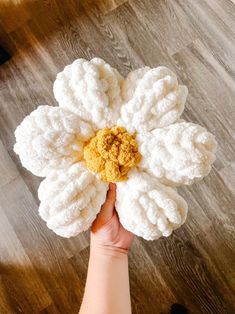 a person holding up a white flower on top of a wooden floor