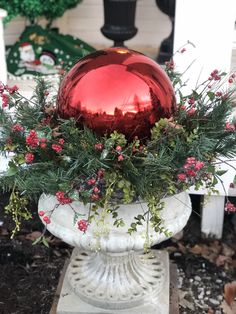 a red glass ball sitting on top of a white vase filled with flowers and greenery