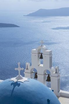 the bell tower is white and blue with bells on it's sides, overlooking the ocean