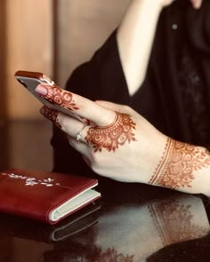 a woman with henna on her hand holding a cell phone next to a book