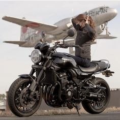 a woman sitting on a motorcycle taking a photo with an airplane in the back ground