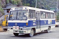 a blue and white bus driving down a street next to a tall mountain covered in trees