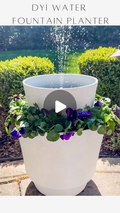 a large white planter filled with purple flowers and water pouring out of it's top