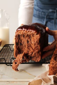 a person holding a piece of cake with chocolate frosting on it and cooling rack