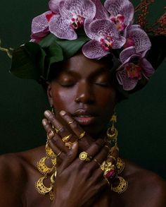 a woman with flowers on her head and jewelry around her neck, holding her hands to her chest