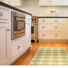 a kitchen with white cabinets and an area rug in front of the stove top oven