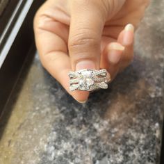 a woman's hand holding an engagement ring in front of her face on a granite countertop