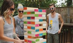 three people standing around a table with a giant block tower on it's side