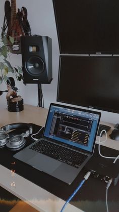 an open laptop computer sitting on top of a desk next to headphones and speakers