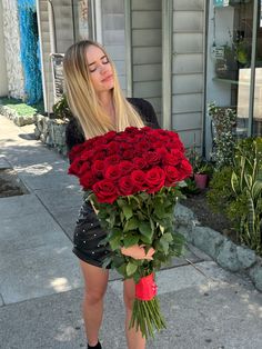 a woman holding a large bouquet of roses on the sidewalk in front of a building