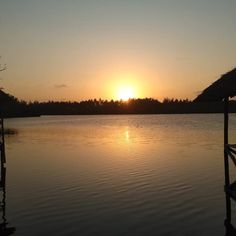 the sun is setting over a lake with trees in the background and thatched umbrellas on either side