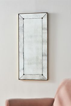 a mirror hanging on the wall above a couch in a room with a pink chair