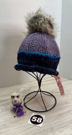 Cozy, handmade, winter hat/beanie, is ready-to-ship and ready-to-wear.  This blue, lavender, and teal beanie features a 5" gray, faux fur, removable PomPom.  Made of a fine wool blend yarn, this beanie must be hand washed and dried flat to preserve its softness and durability.  The hat measures 9" across and 9" tall allowing the wearer to pull it down over the ears or roll it up depending on the required warmth.  As with any handmade item, minor flaws and imperfections are inherent to its construction which adds a unique charm to the finished piece. Winter Hats Beanie, Christmas Deals, Unique Charms, Faux Fur, Caps Hats, Hand Knitting, Pom Pom, Accessories Hats, Winter Hats