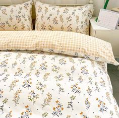 a white bed with yellow and orange flowers on the comforter next to a desk