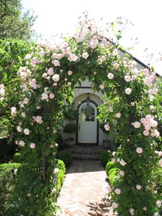 a white door surrounded by pink flowers and greenery on the side of a house